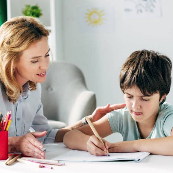 Female teacher practising writing with young student boy