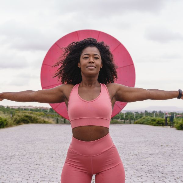 Woman in pink activewear, arms outstretched, smiling.