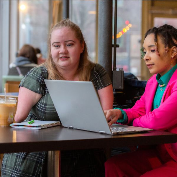 Two students collaborating on a laptop at a cafe.