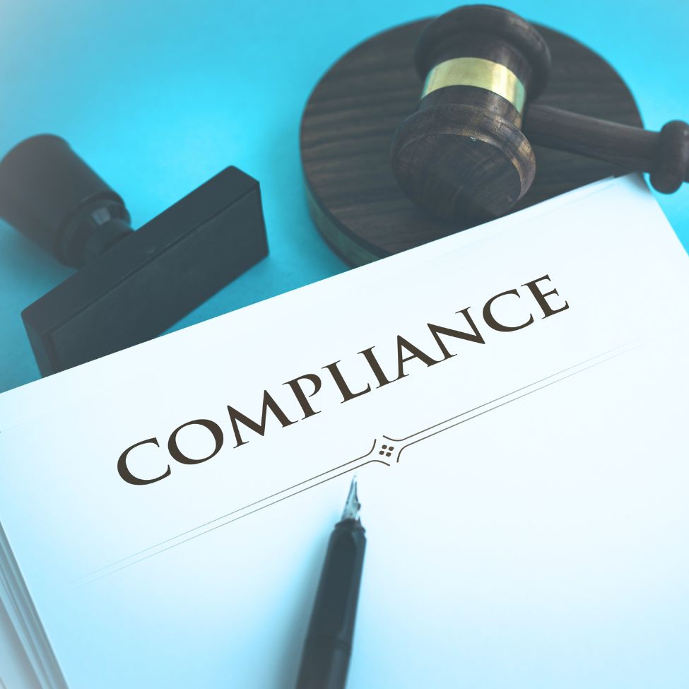 The word "COMPLIANCE" on a document next to a judge's gavel, stamp, and pen on a blue background.