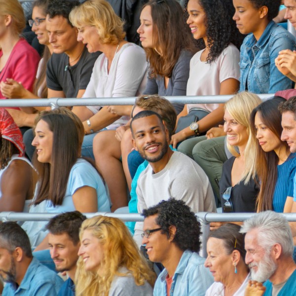 A diverse crowd of people sitting in stadium seating, representing the public audience at a sporting or community event.