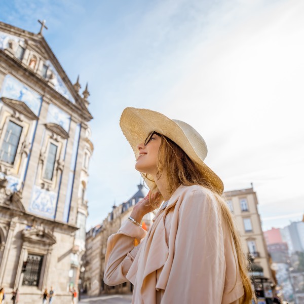 A young woman in a sun hat looking up at the intricate architecture of a historic European cathedral against a bright sky.